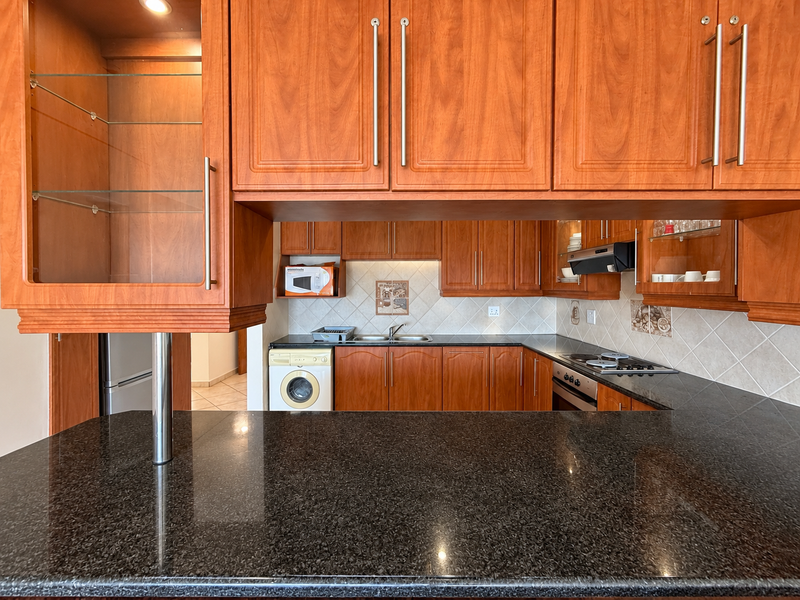 A functional kitchen featuring dark granite countertops, warm-toned wooden cabinetry, built-in cooking appliances, and a tiled backsplash with integrated storage solutions.