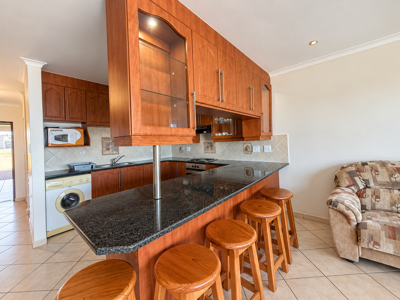 Open-plan kitchen featuring wooden cabinetry, granite countertops, and a breakfast bar, seamlessly integrated with the living area and tiled flooring throughout.