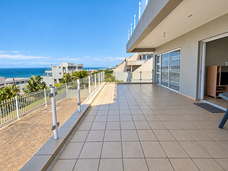 Spacious tiled balcony featuring a modern glass balustrade and expansive ocean views, accessible via large sliding doors.