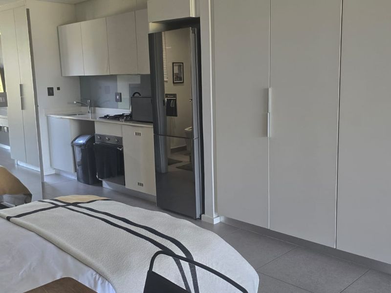 Modern open-plan studio apartment featuring a compact kitchenette with built-in cabinetry, sleek tiled flooring, and direct access to an outdoor patio area.