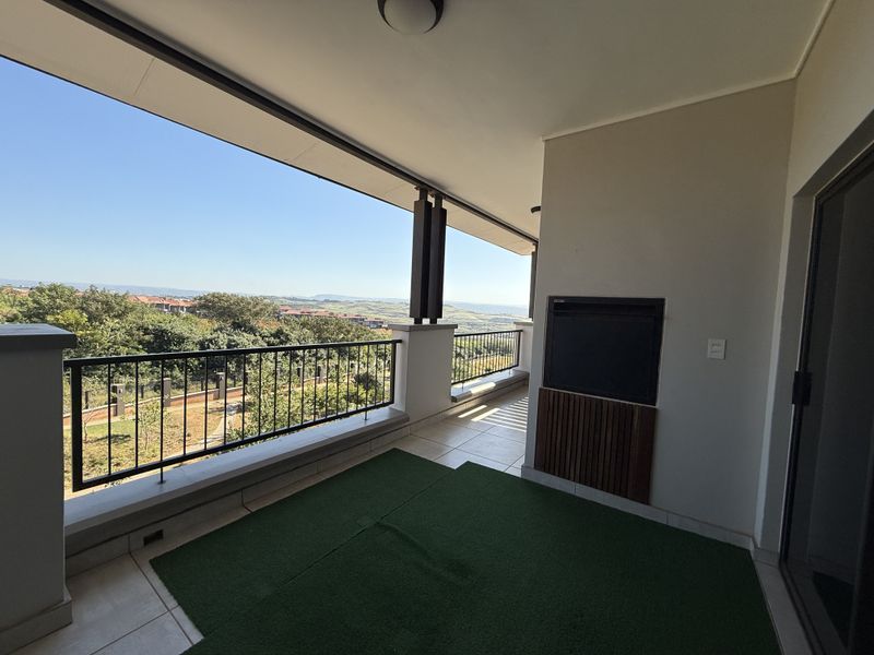 Spacious covered balcony featuring a built-in braai, metal balustrade, and scenic views, providing an ideal space for outdoor entertaining.