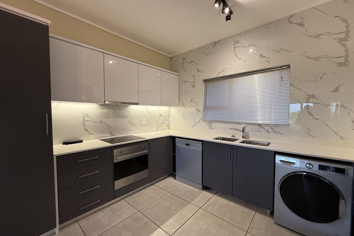 Modern kitchen featuring high-gloss cabinetry, marble-look splashbacks, integrated appliances, and sleek track lighting, offering a clean and contemporary aesthetic.