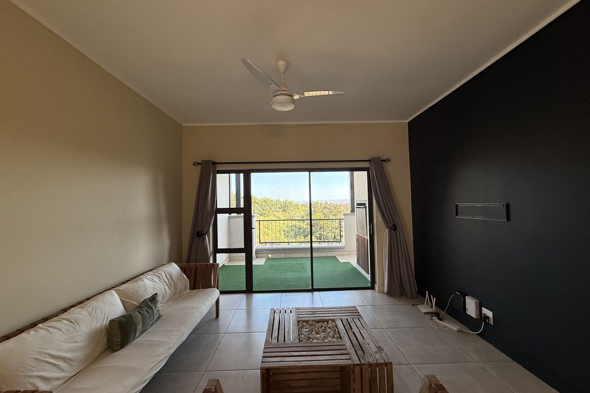 A bright living room featuring tiled floors, a ceiling fan, and large sliding glass doors that open onto a private balcony with scenic views.