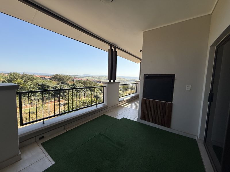 Spacious covered balcony featuring a built-in braai, metal balustrade, and expansive elevated views of the surrounding landscape.