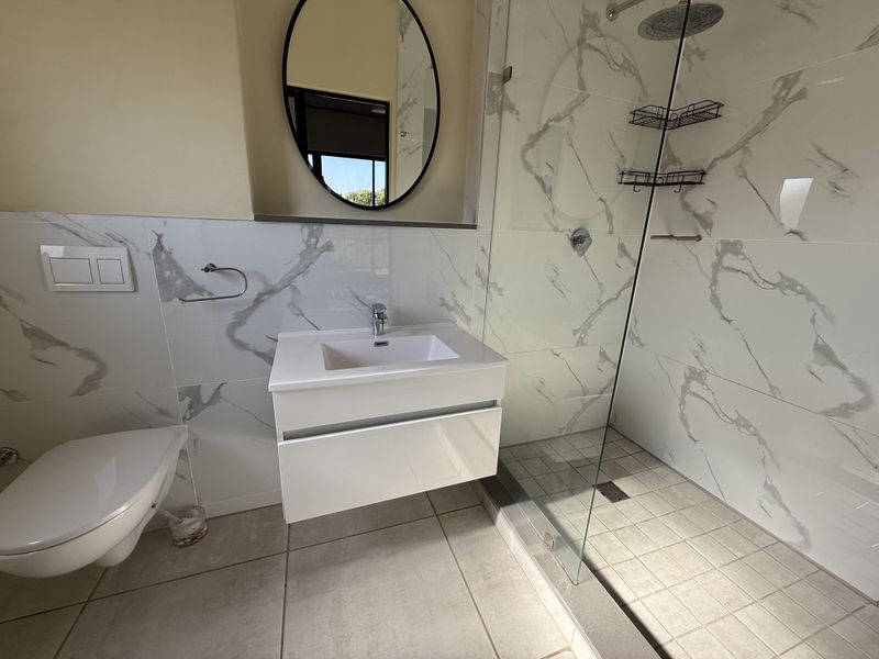 Modern bathroom featuring a wall-mounted vanity, marble-look wall tiling, a glass-enclosed shower with a rain shower head, and a wall-hung toilet.