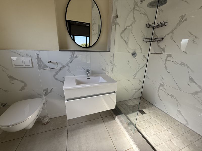 Modern bathroom featuring a wall-mounted vanity, wall-hung toilet with concealed cistern, and a spacious walk-in shower with marble-look tiling.