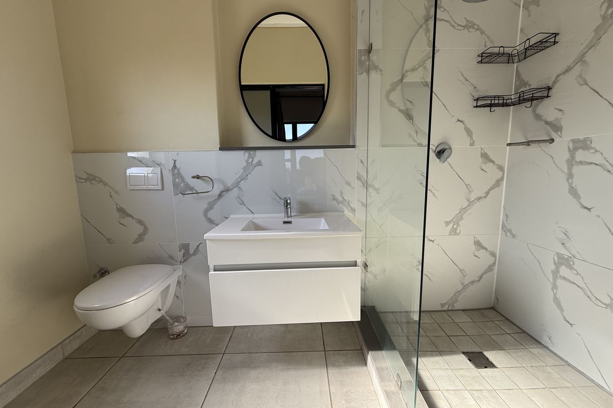 Modern bathroom featuring a floating vanity, wall-mounted toilet, and a spacious walk-in shower with marble-look tiling and a glass enclosure.