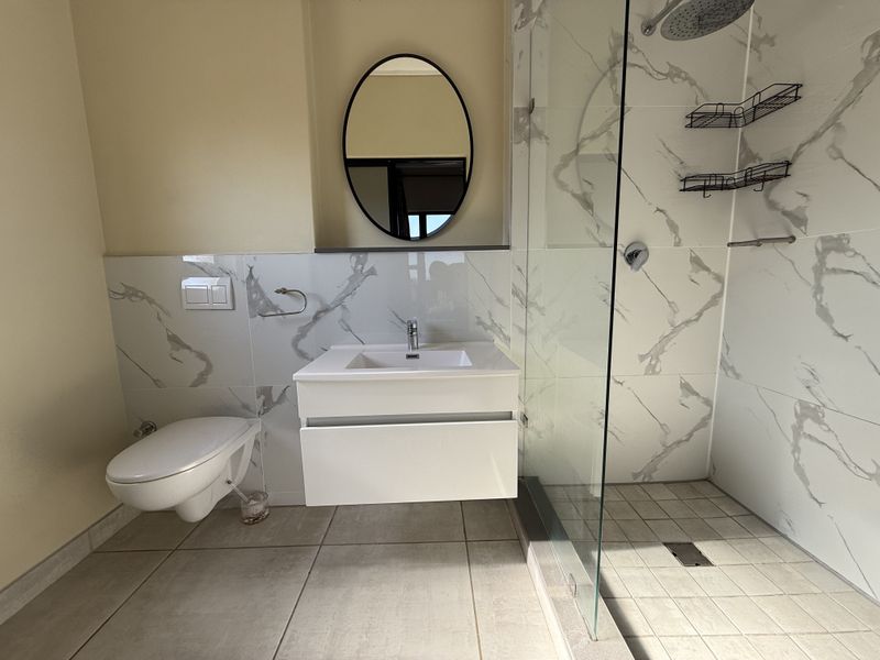 Modern bathroom featuring a floating vanity, wall-mounted toilet, and a spacious walk-in shower with marble-look tiling and a glass enclosure.