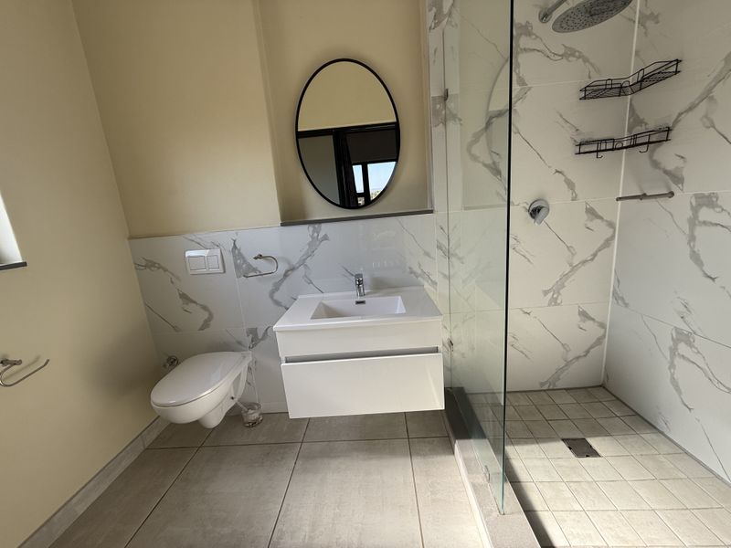 Modern bathroom featuring a floating vanity, wall-mounted toilet, and a spacious walk-in shower with marble-look tiling and high-quality fixtures.