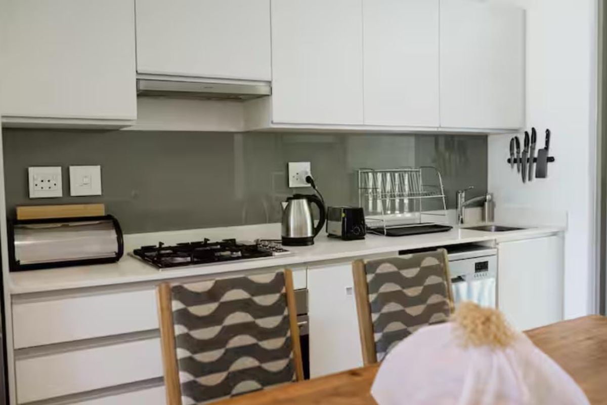 Modern kitchen featuring white cabinetry, stone countertops, a gas hob, extractor fan, and a sleek glass splashback.