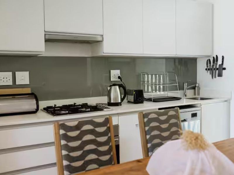 Modern kitchen featuring white cabinetry, stone countertops, a gas hob, extractor fan, and a sleek glass splashback.