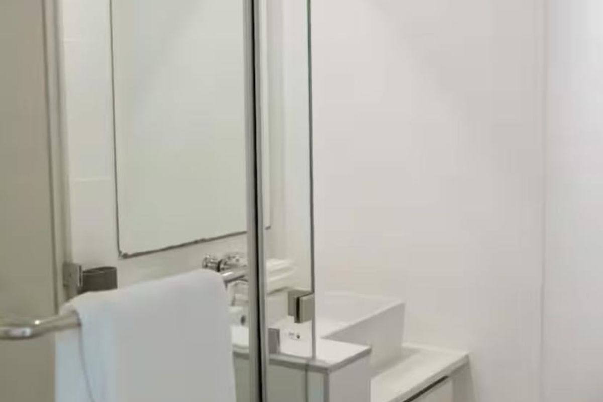 A modern, minimalist bathroom featuring a glass shower enclosure, a sleek vanity cabinet with a vessel sink, and a wall-mounted mirror.