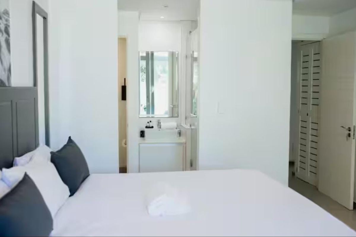 A bright bedroom featuring an en-suite bathroom with a built-in vanity and a louvered door leading to a closet or storage area.
