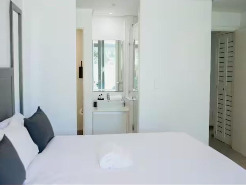 A bright bedroom featuring an en-suite bathroom with a built-in vanity and a louvered door leading to a closet or storage area.