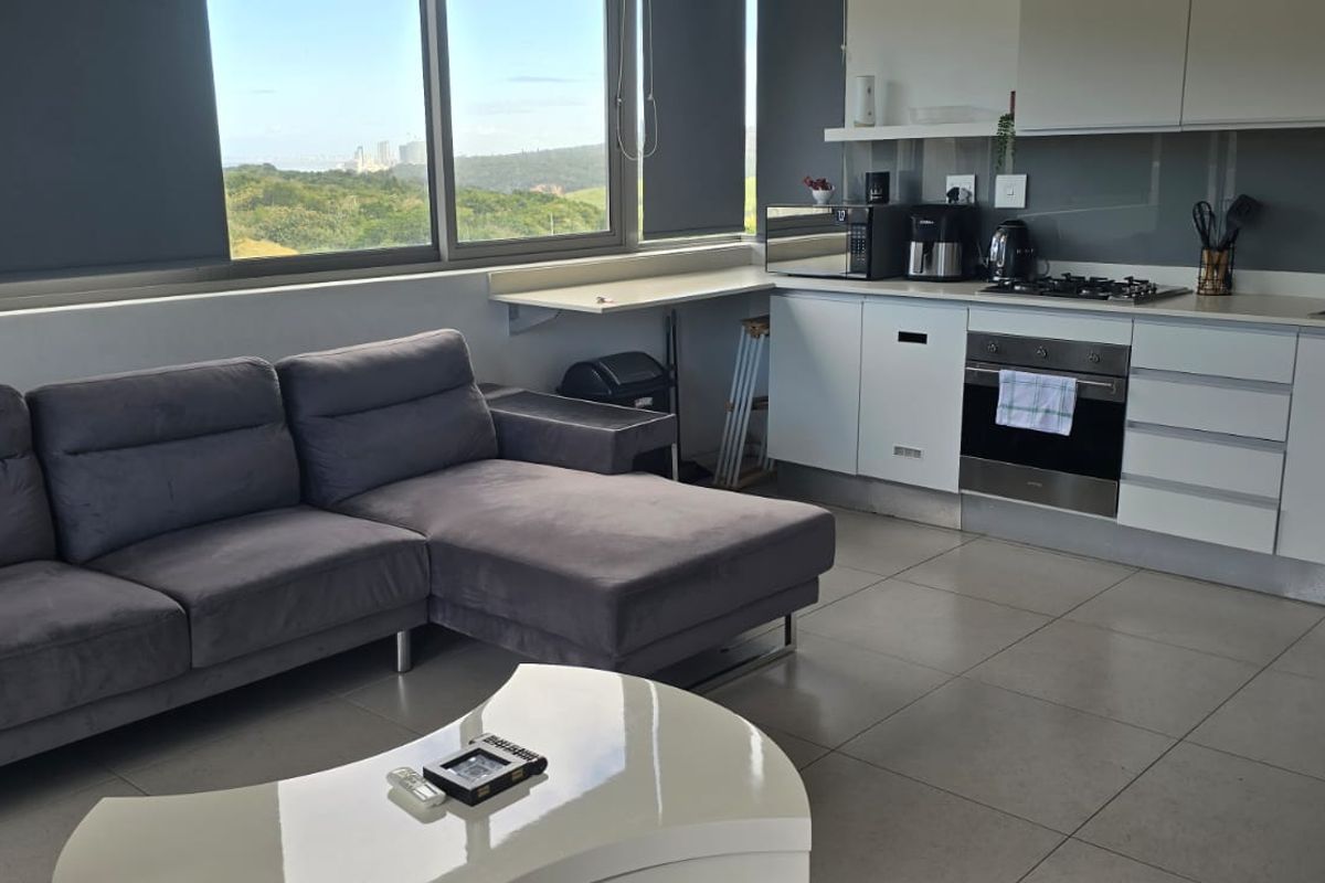 Modern open-plan living area featuring a sleek kitchen with built-in appliances, tiled flooring, and large windows offering expansive views.