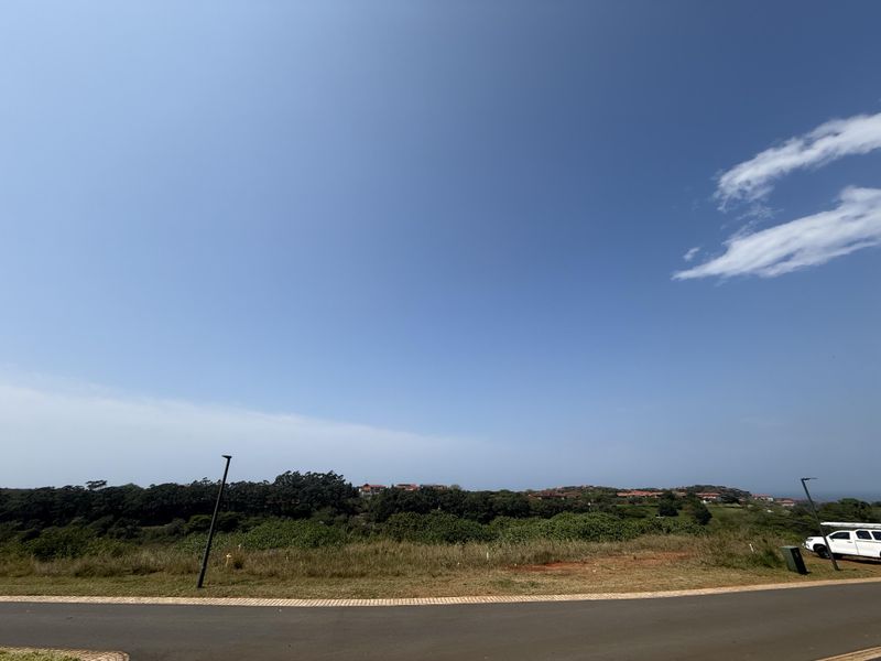 A wide-angle view of the vacant residential land, featuring a paved road in the foreground and natural coastal landscape in the distance.