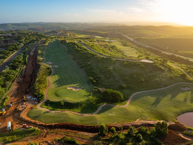 An aerial view of a residential golf estate development featuring manicured fairways, natural landscape, and ongoing site preparation work.