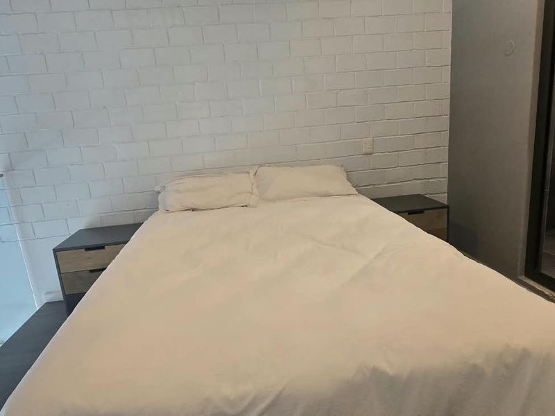 A modern bedroom featuring an exposed white brick wall, glass balustrade, and direct access to an en-suite bathroom.