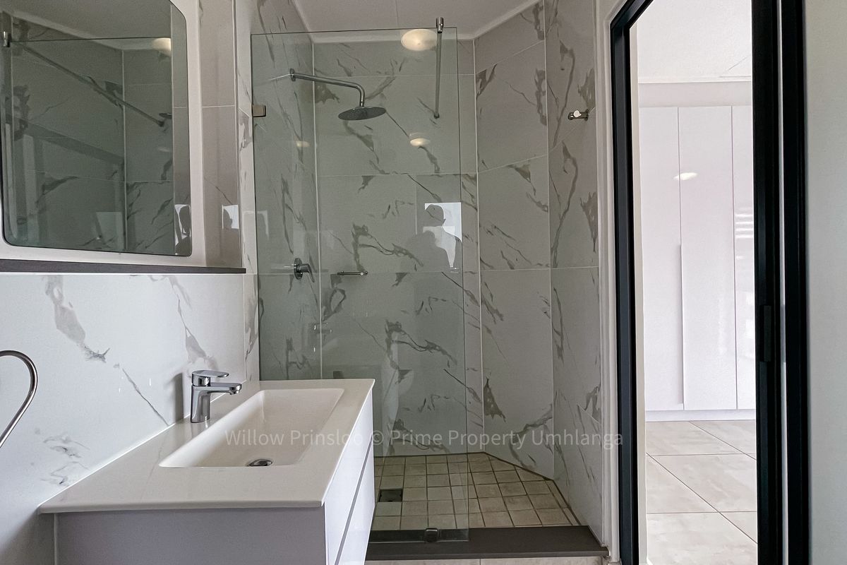 Modern bathroom featuring a sleek vanity, marble-look wall tiles, and a glass-enclosed shower with a rainfall shower head.