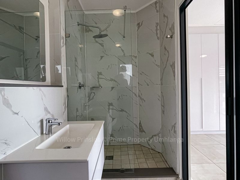Modern bathroom featuring a sleek vanity, marble-look wall tiles, and a glass-enclosed shower with a rainfall shower head.