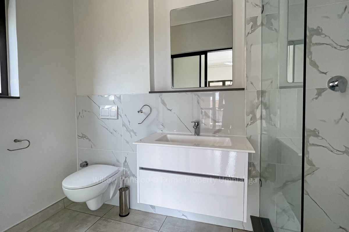 Modern bathroom featuring a wall-mounted toilet, sleek vanity with integrated sink, and a glass-enclosed shower with elegant marble-look wall tiling.