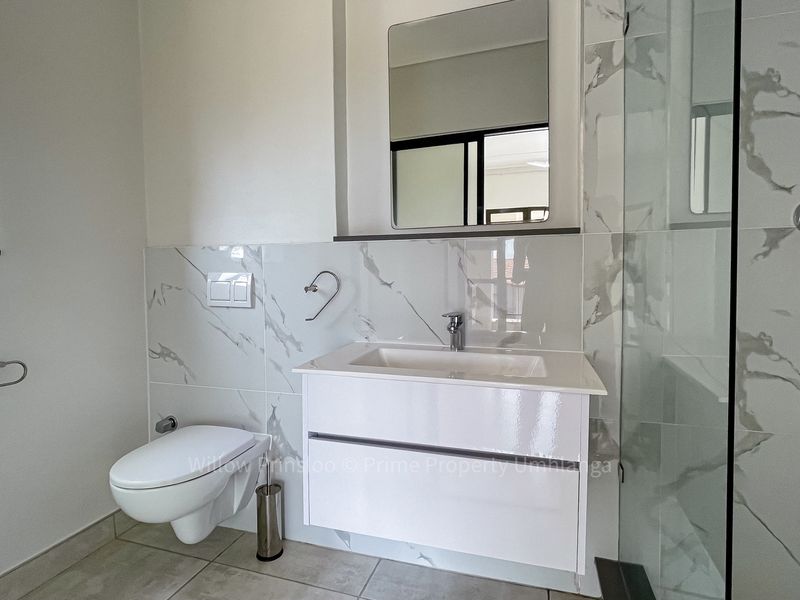 Modern bathroom featuring a wall-mounted toilet, sleek vanity with integrated sink, and a glass-enclosed shower with elegant marble-look wall tiling.