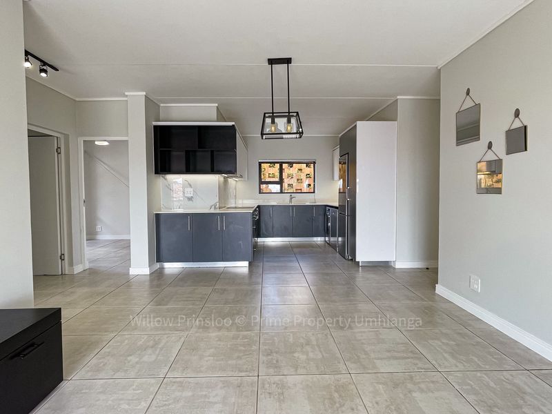 Modern open-plan living area featuring tiled floors, contemporary kitchen cabinetry with stone-look backsplash, and stylish pendant lighting.
