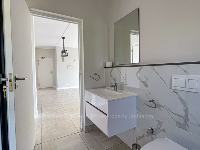Modern bathroom featuring a wall-mounted vanity, marble-look tiled walls, and a concealed cistern toilet, with a view into the adjacent living area.