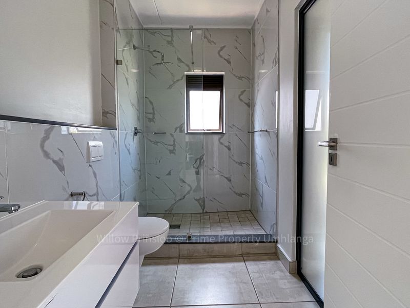 Modern bathroom featuring a walk-in shower with glass screen, marble-look wall tiles, and a sleek wall-mounted vanity unit.