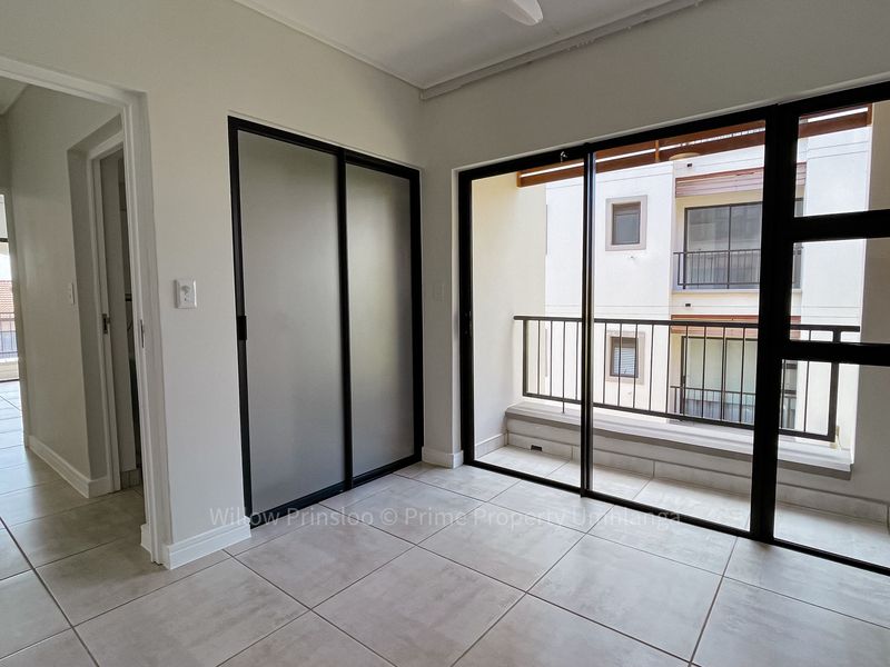 A bright, empty bedroom featuring tiled flooring, a built-in sliding door wardrobe, and direct access to a private balcony through large glass sliding doors.