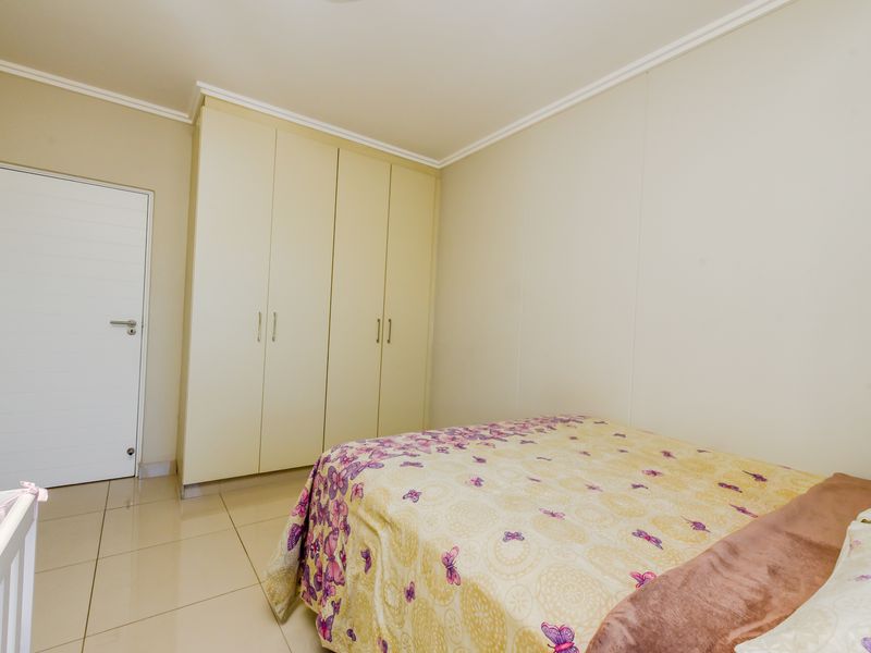 A well-maintained bedroom featuring neutral tiled flooring, built-in cupboards, and clean wall finishes, offering a bright and functional living space.