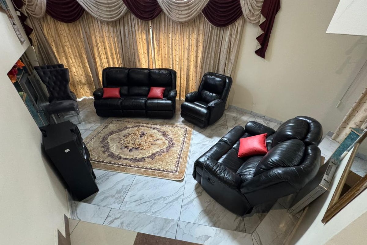 A living room area featuring large windows with decorative curtains and tiled flooring, viewed from an elevated perspective.
