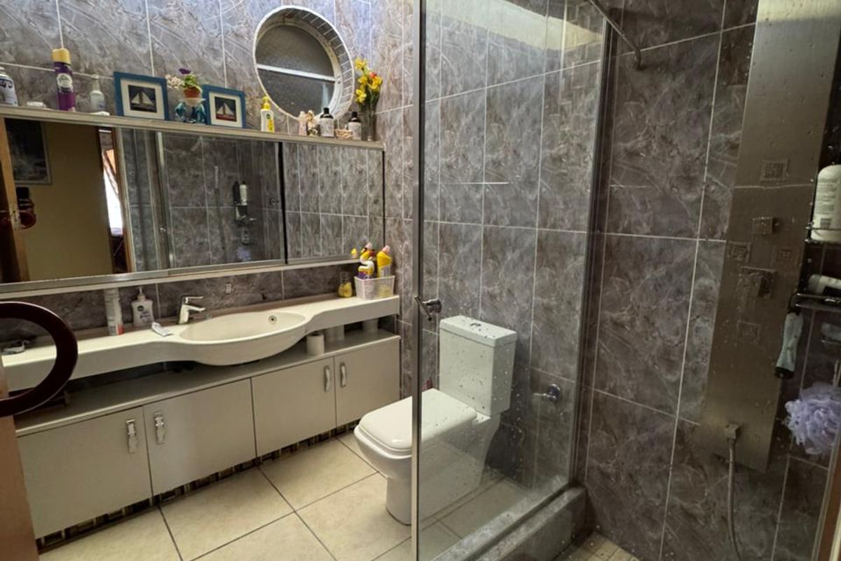 A functional bathroom featuring a glass-enclosed shower, vanity with integrated basin, large wall mirror, and tiled finishes throughout.