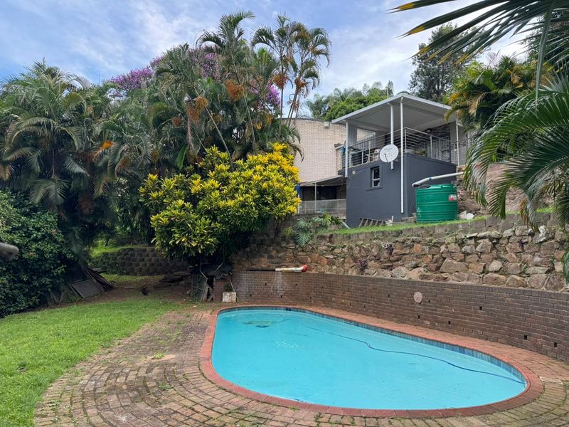 Outdoor pool area featuring a swimming pool, brick retaining walls, and a covered patio structure set within a landscaped garden.