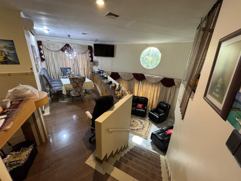Spacious open-plan living and dining area featuring tiled floors, recessed lighting, a unique circular window, and built-in cabinetry, overlooking a lower seating level.