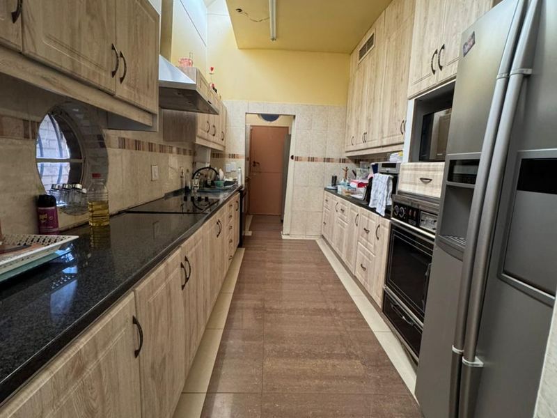 Galley-style kitchen featuring wood-look cabinetry, granite countertops, integrated appliances, and a skylight providing natural light.