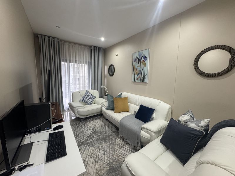 A comfortable living room featuring neutral wall tones, recessed lighting, and a sliding glass door providing access to the balcony.