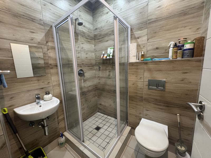 Modern bathroom featuring a glass shower enclosure, wall-mounted toilet, and basin with wood-look tiled walls.