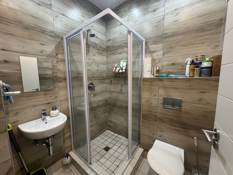 Modern bathroom featuring wood-look wall tiling, a glass shower enclosure, wall-mounted basin, and a wall-hung toilet with a concealed cistern.