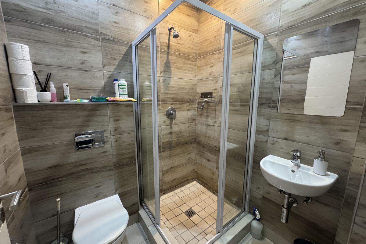 Modern bathroom featuring wood-look wall tiles, a glass shower enclosure, wall-mounted toilet, and a sleek wall-mounted basin.