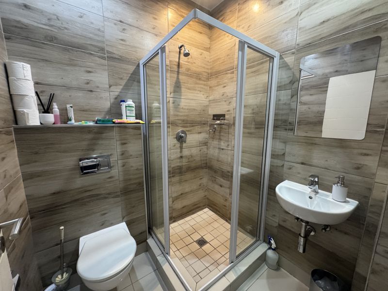 Modern bathroom featuring wood-look wall tiles, a glass shower enclosure, wall-mounted toilet, and a sleek wall-mounted basin.