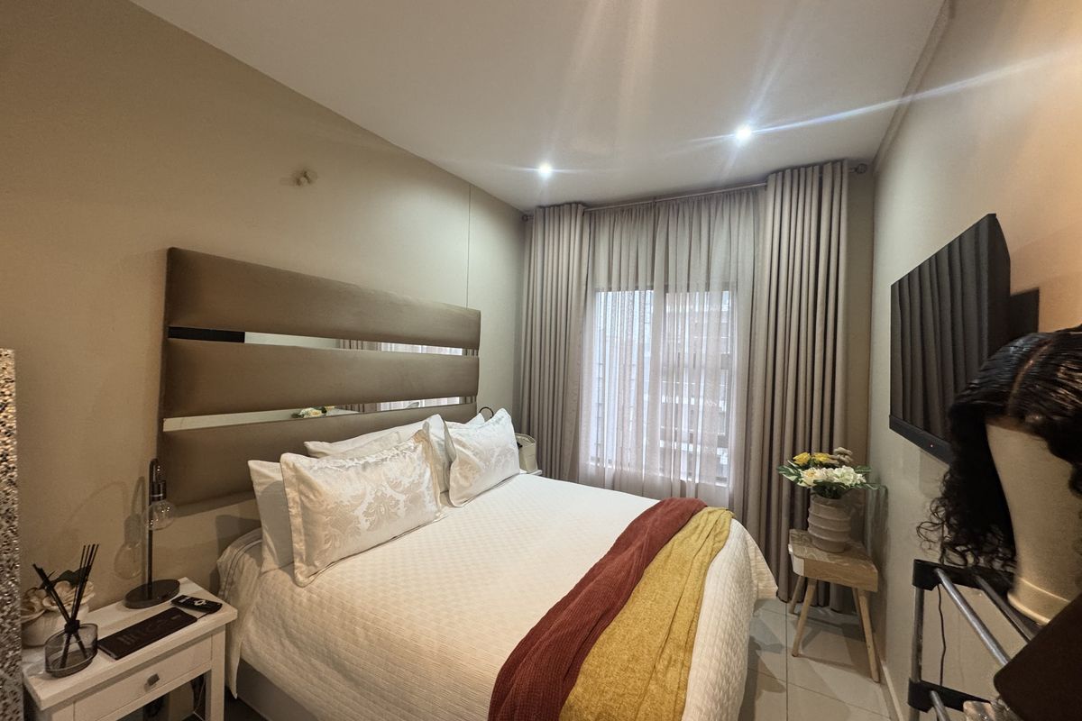 A well-maintained bedroom featuring neutral wall tones, recessed downlighting, and floor-to-ceiling curtains providing natural light control.