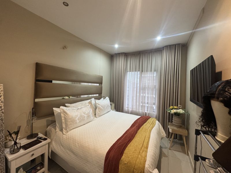A well-maintained bedroom featuring neutral wall tones, recessed downlighting, and floor-to-ceiling curtains providing natural light control.