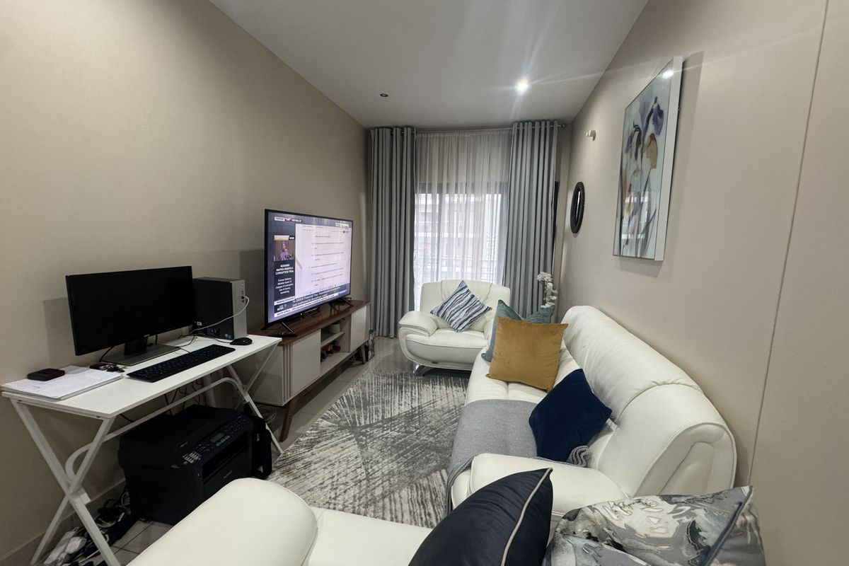 A well-maintained living room featuring neutral wall tones, tiled flooring, and large windows with floor-to-ceiling curtains, providing a comfortable and functional living space.