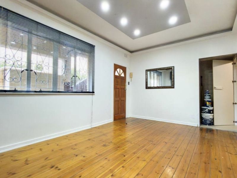 An empty living room featuring polished timber flooring, recessed ceiling lights, and a secure timber entrance door with an intercom system.