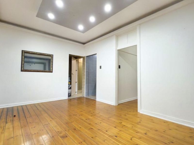 An empty living room featuring polished hardwood flooring, recessed ceiling lighting, and coved detailing, providing a clean and neutral canvas.