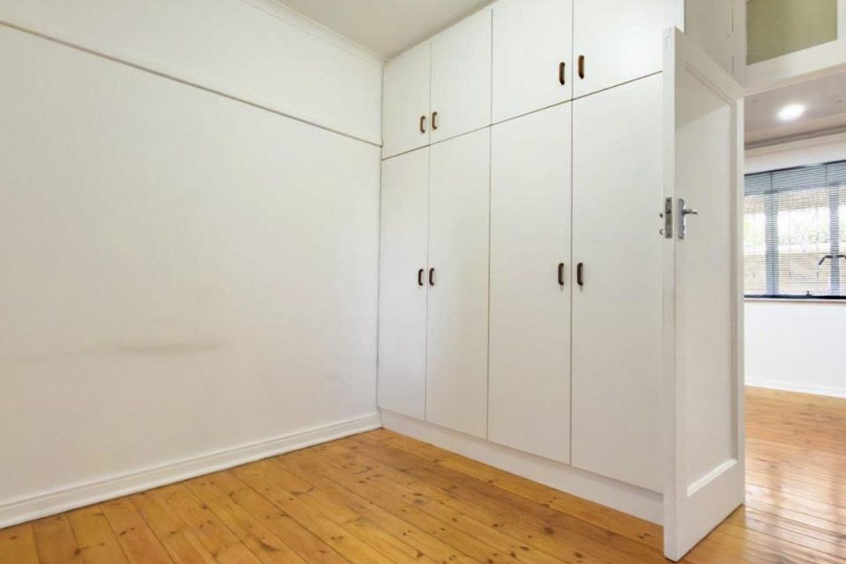 A bright, empty bedroom featuring polished timber flooring and extensive floor-to-ceiling built-in cupboards.