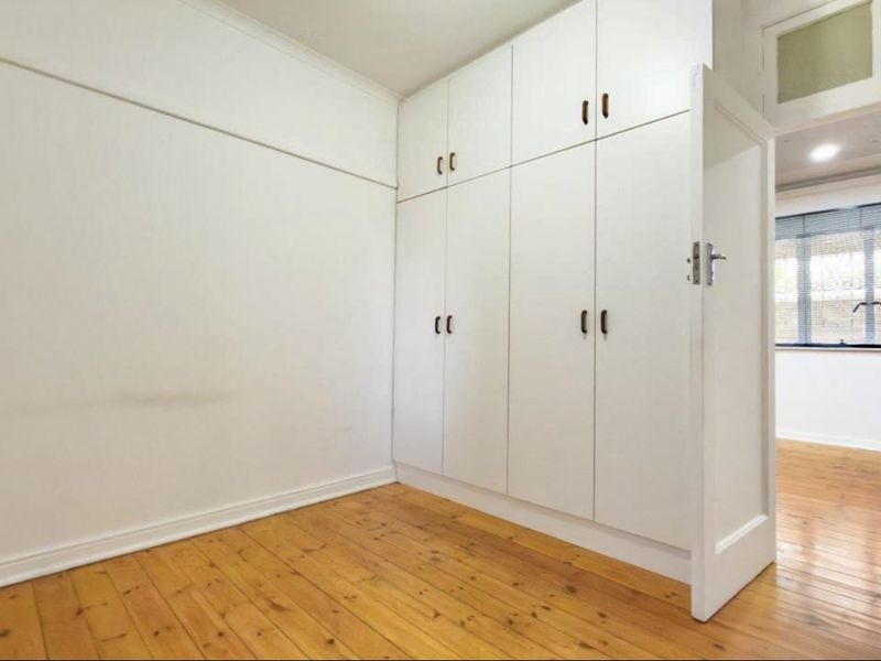 A bright, empty bedroom featuring polished timber flooring and extensive floor-to-ceiling built-in cupboards.