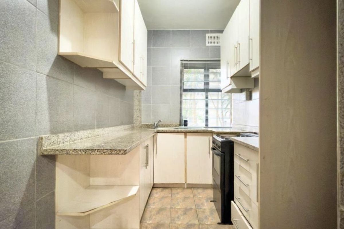 A functional galley-style kitchen featuring granite countertops, ample built-in cabinetry, tiled backsplash, and tiled flooring, providing a clean and practical workspace.