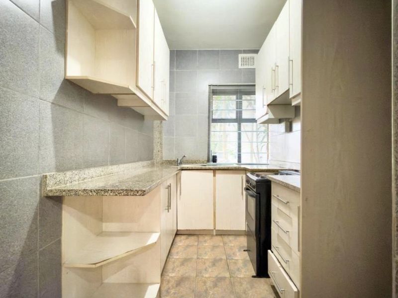 A functional galley-style kitchen featuring granite countertops, ample built-in cabinetry, tiled backsplash, and tiled flooring, providing a clean and practical workspace.